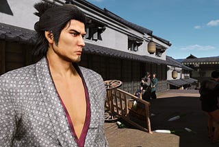 Like a Dragon Ishin’s protagonist Sakomoto Ryoma stands in profile in front of a tipped over cart in the city of Kyo.