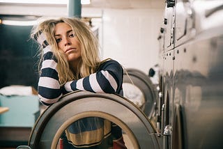 A woman stands behind the open door of a dryer with an annoyed expression on her face.