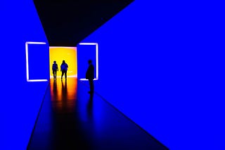 Two persons walks through a blue corridor while one stares at them.