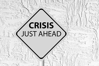 This os a black and white photo of a traffic warning sign saying “Crisis just ahead.”