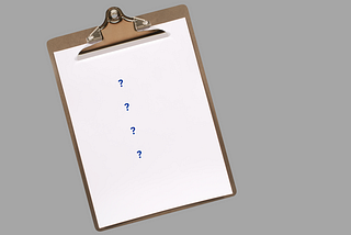 A brown clipboard tilted at an angle on a gray background, containing four blue question marks arranged vertically on white paper.