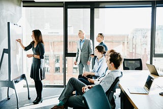 A businesswoman leads a white board session and presentation in a conference room with her colleagues.