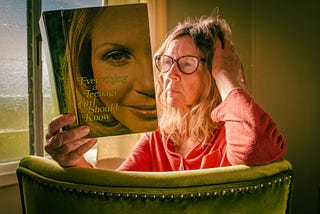 Photo of a late-middle aged woman reading a book called Everything a Teenage Girl Needs to Know