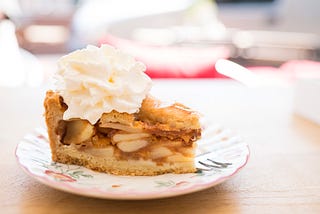 A picture of a slice of apple pie with whipped cream.