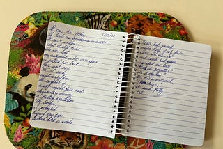 A handwritten poem in a spiral-bound notebook on a multicoloured mat.