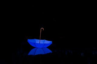 Upside down bright blue umbrella on ground, the rest of image is totally black.