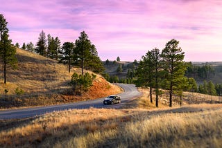My Mazda sits on a small section of pavement between the trees and grasses of the Black Hills as the sun sets just out of camera’s view.