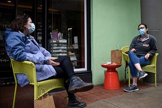 Friends wearing face masks practice social distancing as they chat in front of a shop during the outbreak of COVID-19.