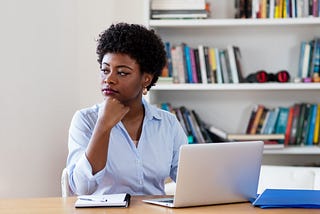 An African American businesswoman looking pensive while at home, in front of her laptop.