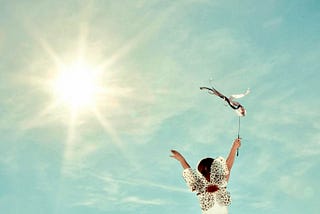 child wearing sparkling wings and holding a streamered baton high against a blue sky and brilliant sun