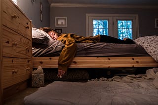 Disheveled young woman laying in bed holding tissue and tissue box.