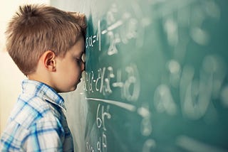 A child resting his head and face on the blackboard