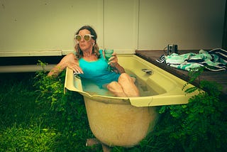 A woman relaxing in an old bathtub outdoors, holding a glass of wine