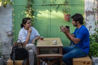 A man and a woman sitting at a coffee table. The woman is listening as the man is conversing over coffee.