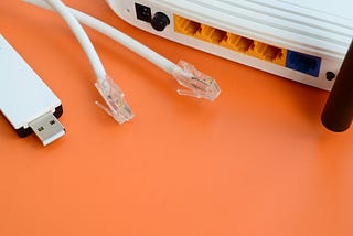 A partial view of ethernet network connection plugs, the port-side of a router,  and a USB stick against an orange background.