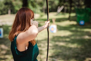 Woman aiming with a bow and arrow at a target.