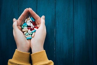 Two hands holding a large amount of various pills.