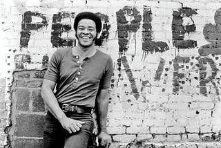 Bill Withers poses for a portrait against a brick wall circa 1973.