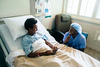 A smiling nurse jokes with a boy patient in a hospital bed.