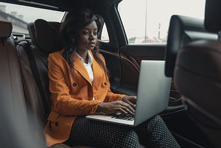 A woman works on a laptop in the back seat of her car.