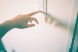 A washed out grainy image of a person touching a light switch.