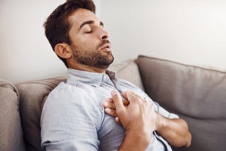 A young man holding his chest in pain while relaxing on a sofa at home.
