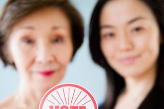 Asian mother and daughter holding a VOTE sticker.