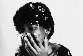Black & white image of a woman holding her face in her hands. She might be laughing or crying.