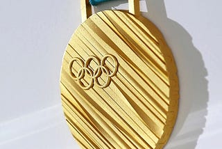 Close-up of a gold medal from the 2018 PyeongChang Olympics, showing a ridge-textured golden surface upon which the Olympic rings are set.