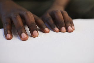 A closeup photo of a black person’s hands reading Braille.