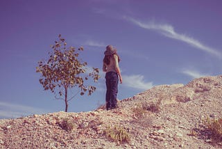 A photo of a woman standing on top of a dune and looking away to the sky