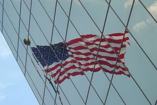American flag reflected on the glass surface of a building, distorted.