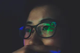 Reflection on glasses of woman working late at night on computer.