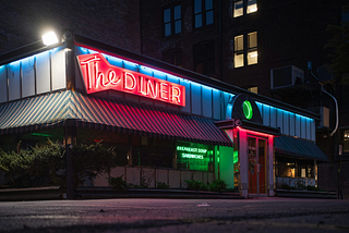 A diner at night, reflections in the puddles after a storm