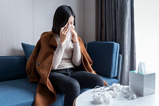 A woman sneezes into a tissue and wipes her nose.