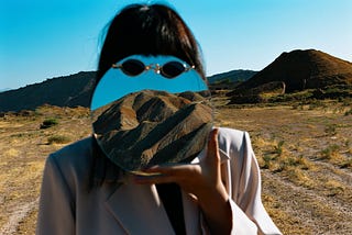 Woman with mirror to face in the desert
