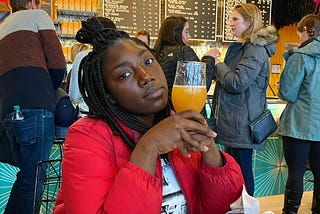 Nikita Richardson holding a glass of orange juice in a cafe, with people in line behind her.
