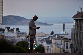 Black businessman checking phone while on the street in San Francisco in the evening.