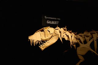 An large origami T-rex fossil, with a plaque that says “T-rex: Gilbert”