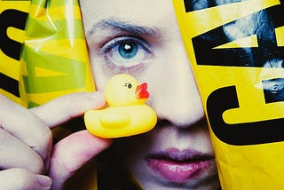 A person holding up a tiny yellow duck in front of their face