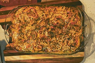 Overhead shot of a casserole topped with crispy bits in a clear casserole dish on a wooden cutting board.