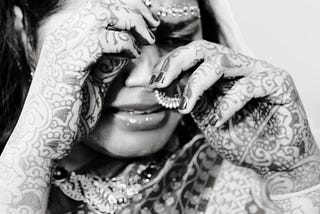 A black-and-white photo of an Indian bride crying, her hands wiping her tears.