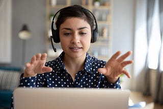 A photo of a South Asian woman talking on the mic on a video conference call.