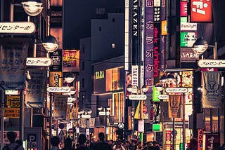 A busy street with neon signs, filled with shops and shoppers.