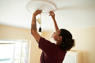 Woman installing light bulb on ceiling while renovating home.