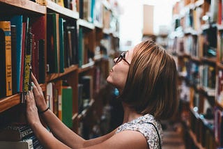 Woman in bookstore looking up at a higher shelf full of books.