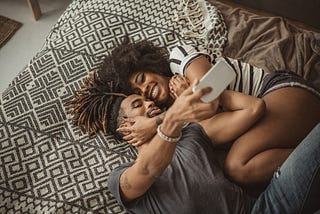 A photo of a happy couple taking a selfie while laying on a bed.