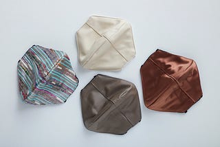 4 shimmery cloth facemasks. Three are solid-colored neutrals and one has sequined blue, purple, and gray stripes.