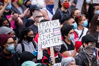 A protestor in a crowd holds up a sign that says “TRANS BLACK LIVES MATTER.”