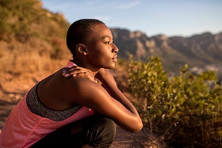 A photo of a peaceful black woman looking out at the view while taking a break on a hike.